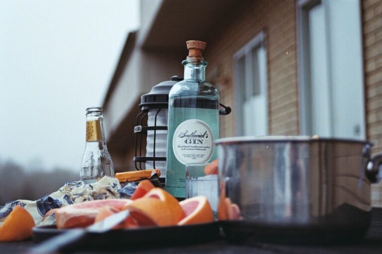A rustic outdoor setting with gin, grapefruits, and a pot on a table.