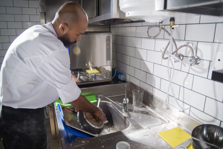 A chef cleans kitchen utensils in a stainless steel sink, maintaining hygiene standards.